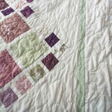 Detailed view of quilt border with soft green binding and cream background highlighting fine quilting stitches