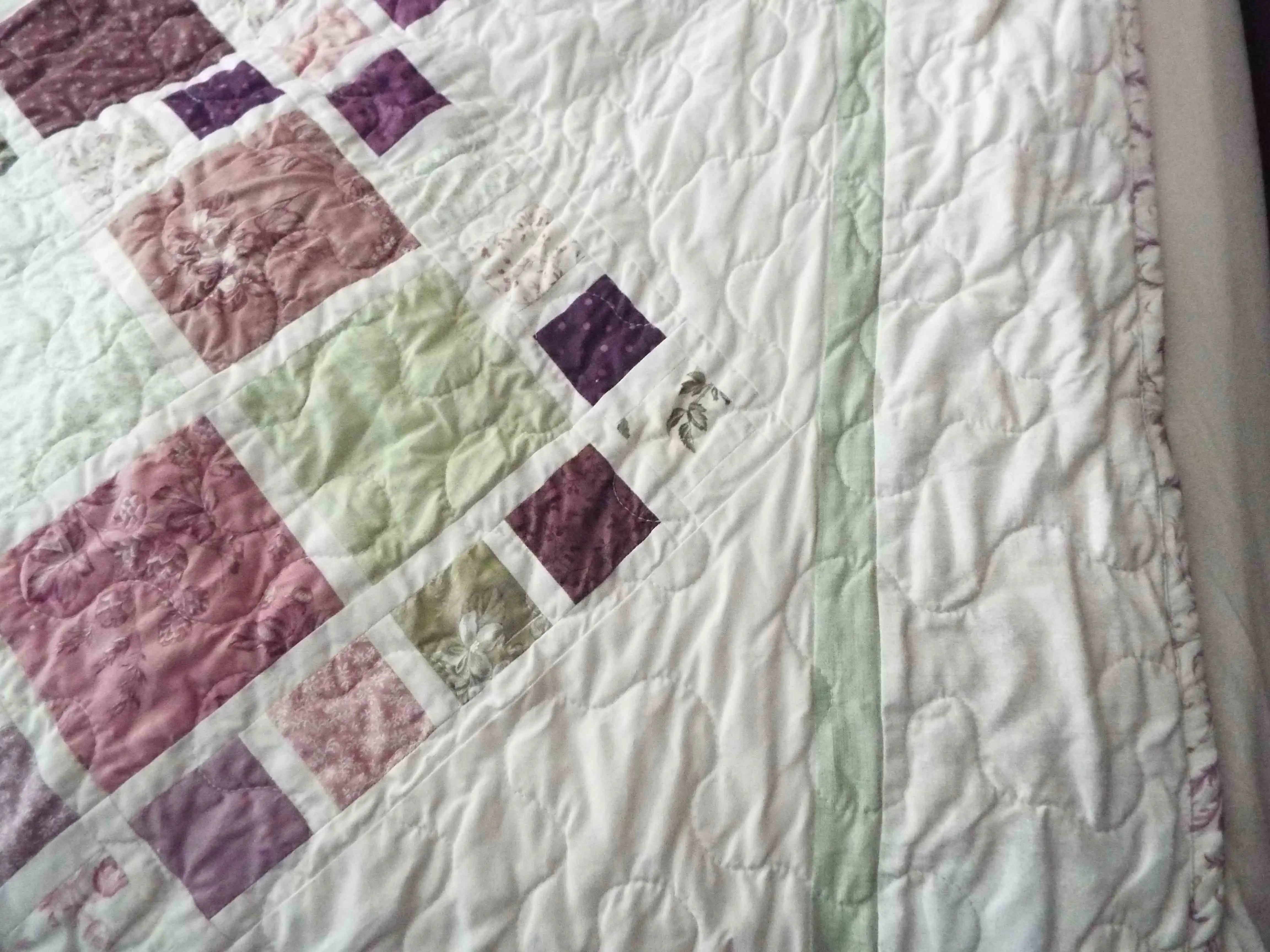 Detailed view of quilt border with soft green binding and cream background highlighting fine quilting stitches