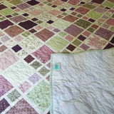 Surface detail of lavender and sage quilt, showing quilted stitching pattern across cotton squares and backing.