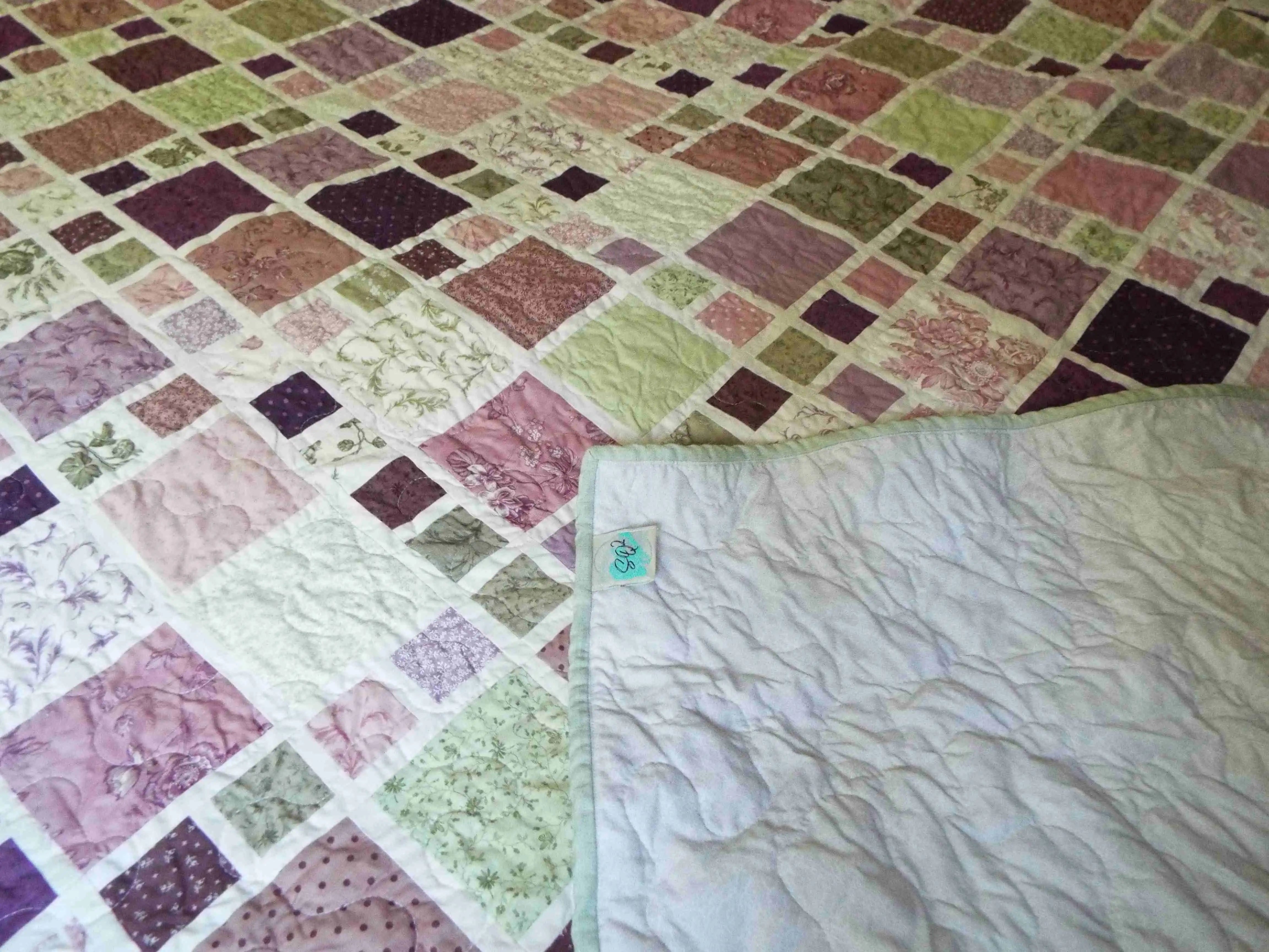 Surface detail of lavender and sage quilt, showing quilted stitching pattern across cotton squares and backing.