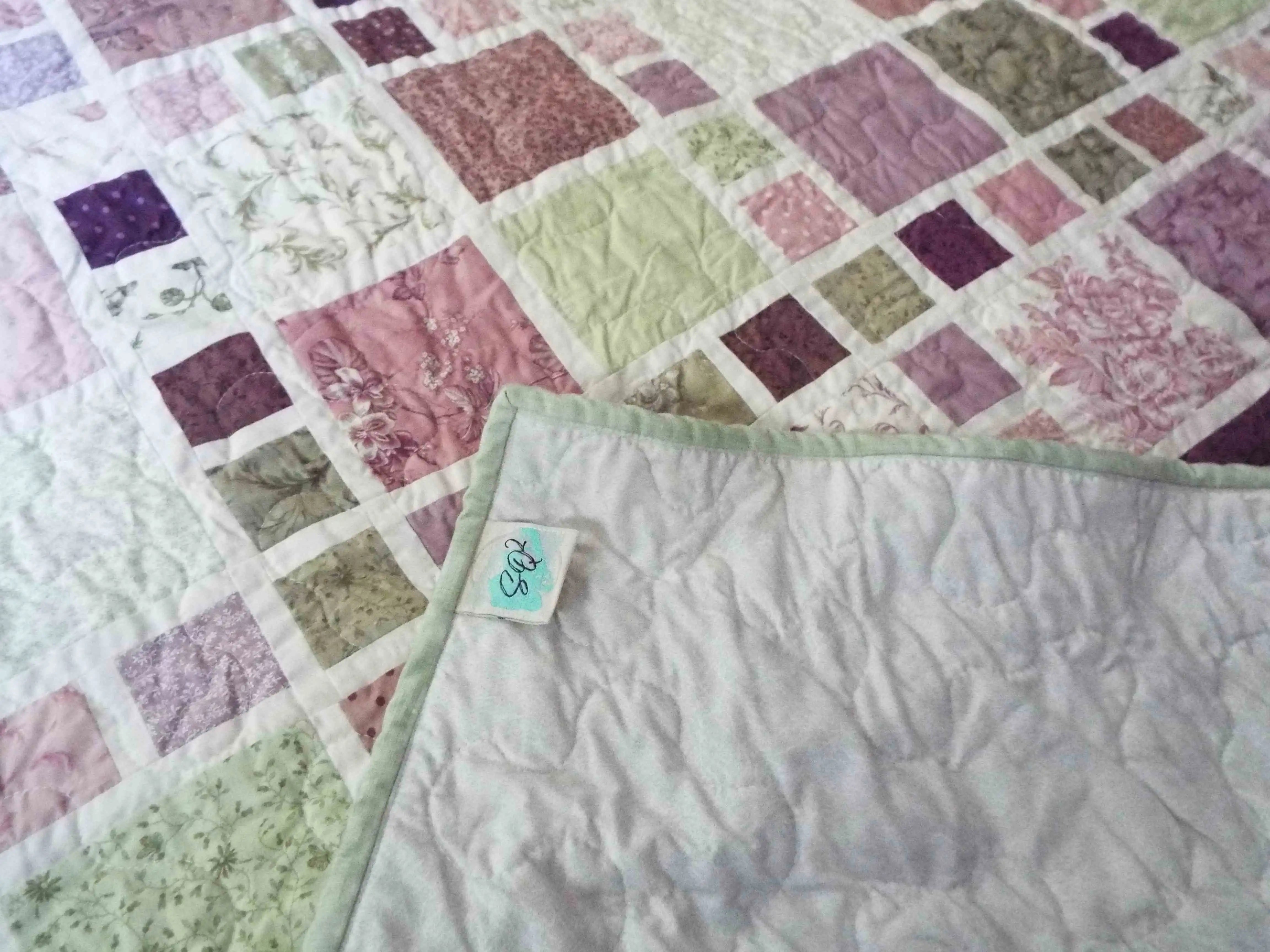 Corner detail of handmade quilt with SQ² Creations fabric label and coordinating backing.