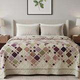 Handmade patchwork quilt in muted purples and greens styled in a modern neutral bedroom with upholstered headboard and botanical wall art.