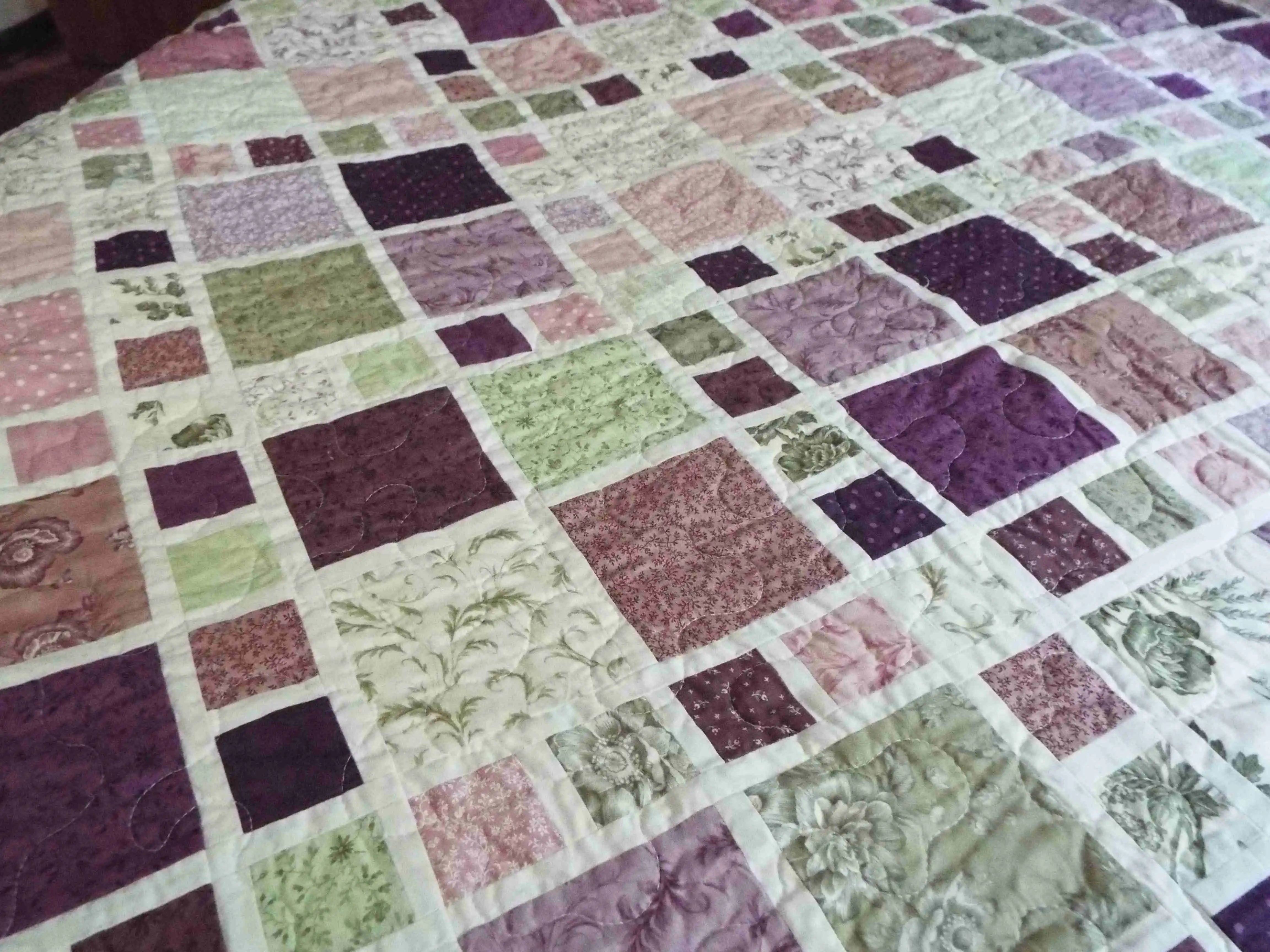 Close-up of lavender and green patchwork squares on handmade king quilt showing intricate stitching and soft cotton texture
