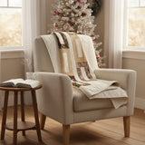 Elegant holiday quilt draped over the back of an armchair with a Christmas tree in the background