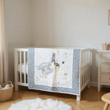 Modern safari-themed baby quilt displayed on white crib with dresser and woven accents in peaceful nursery