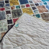 Corner of the Of Ink and Thread King Quilt folded to reveal the soft neutral backing, signature SQ² label, and free-motion quilting pattern.