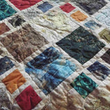 Detail of colorful fabric squares in teal, amber, and olive tones showcasing quilted stitching and fabric texture.