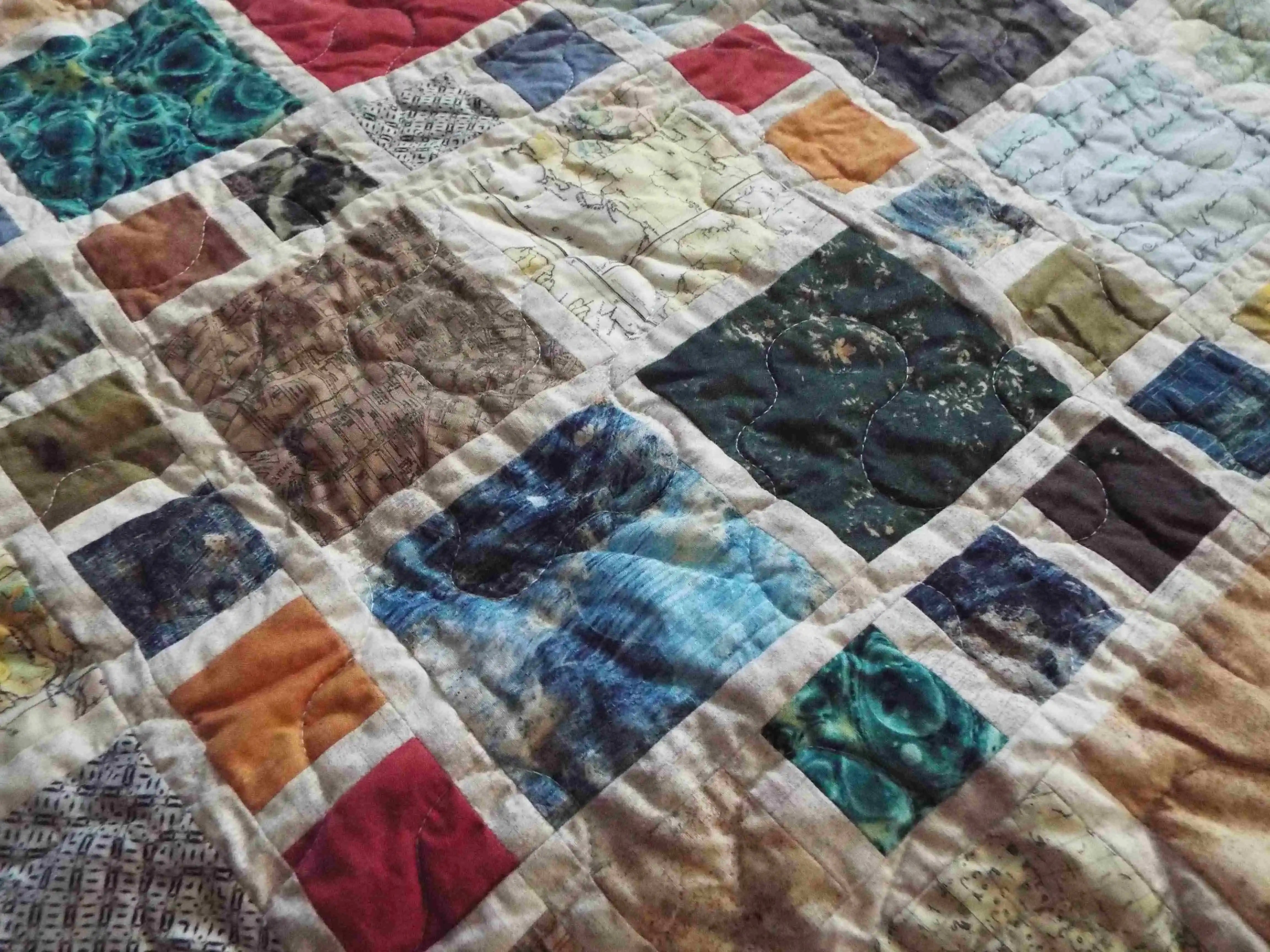 Detail of colorful fabric squares in teal, amber, and olive tones showcasing quilted stitching and fabric texture.