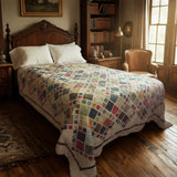 Handmade king quilt in mixed indigo, parchment, and ochre fabrics shown in a heritage-style room with bookshelves and vintage decor.