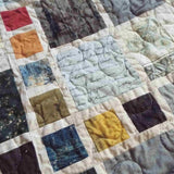 Close-up of fabric blocks featuring script, maps, and vintage-inspired designs stitched together in balanced geometric layout.