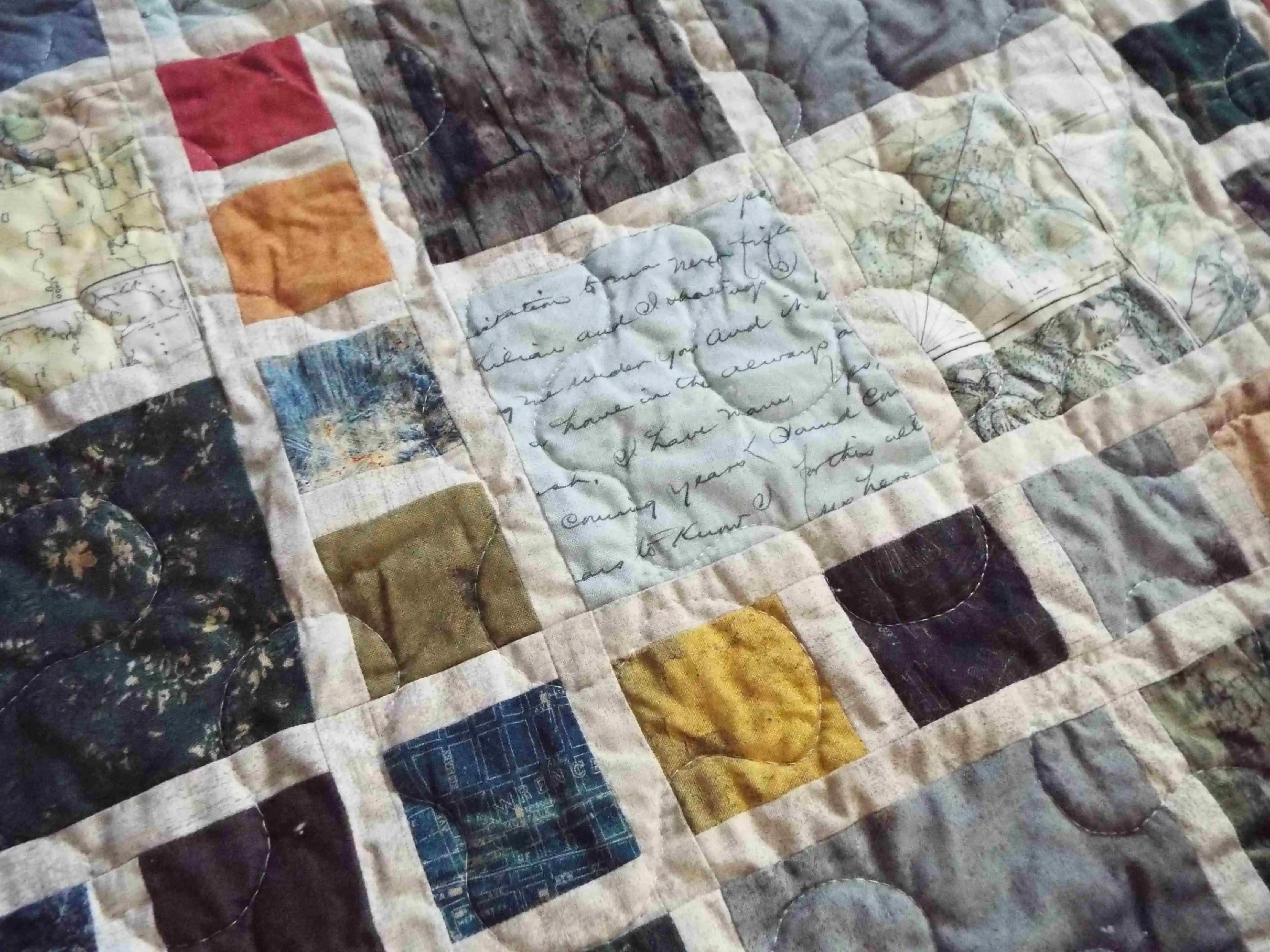 Close-up of fabric blocks featuring script, maps, and vintage-inspired designs stitched together in balanced geometric layout.