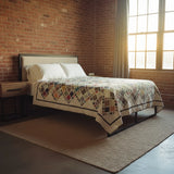 Handmade king quilt in deep indigo, parchment, and rust tones displayed in an industrial loft bedroom with brick walls and natural window light.