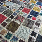 Close view of the Of Ink and Thread King Quilt showing its mosaic-style patchwork in rich blues, greens, reds, and map-inspired prints.
