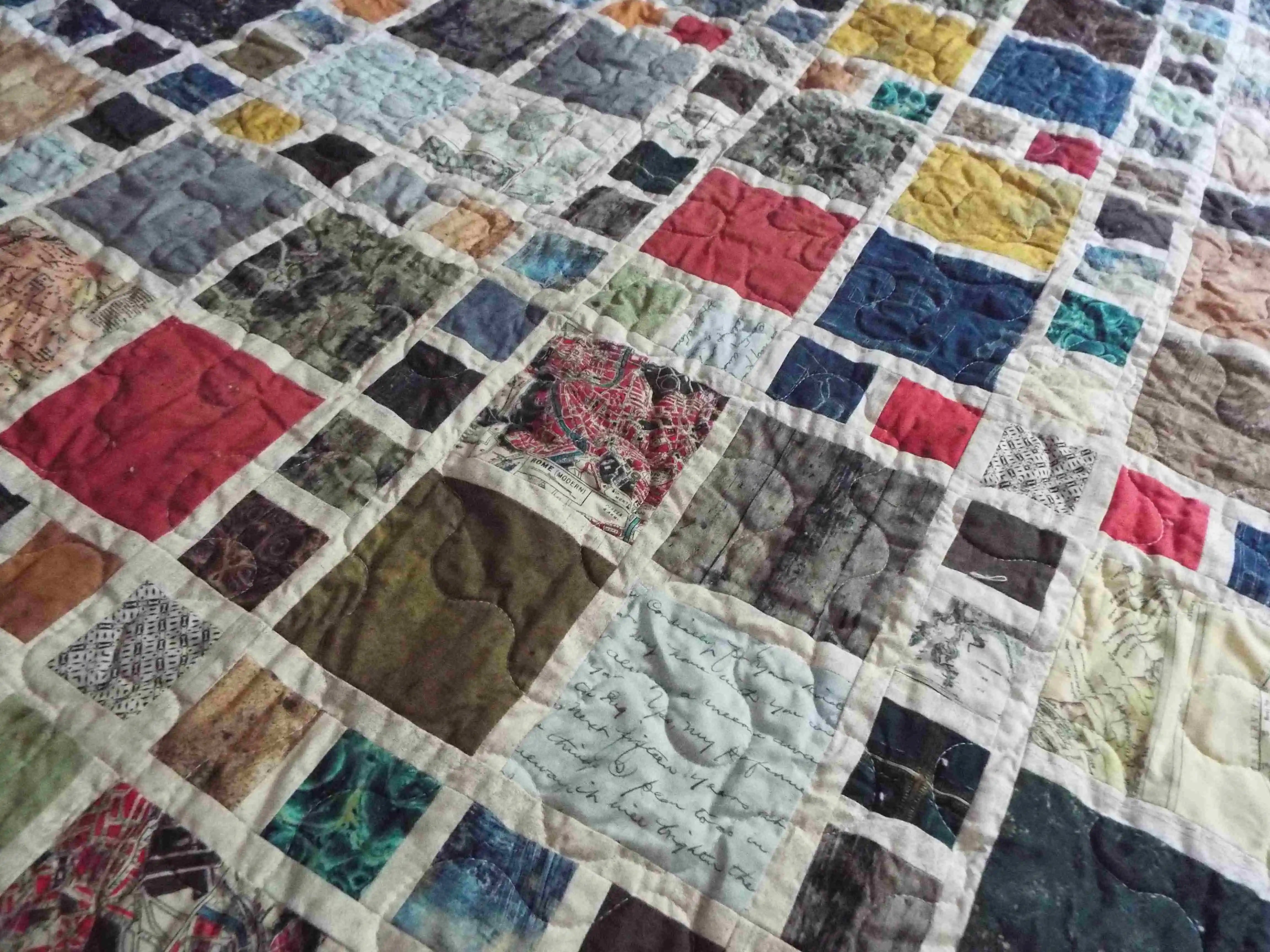 Close view of the Of Ink and Thread King Quilt showing its mosaic-style patchwork in rich blues, greens, reds, and map-inspired prints.
