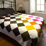 Handmade rainbow patchwork quilt on queen bed with iron headboard and soft morning light through window