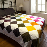 Handmade rainbow patchwork quilt on queen bed with iron headboard and soft morning light through window