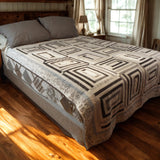 Handmade black and white quilt with rectangular blocks styled on a wooden bed in a cozy farmhouse-inspired bedroom