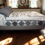 Black and white modern quilt with geometric patchwork draped over a bed in a rustic farmhouse bedroom setting.