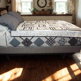 Black and white modern quilt with geometric patchwork draped over a bed in a rustic farmhouse bedroom setting.