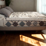 Twin-sized handmade quilt in black and white rectangle design laid flat on a modern upholstered bed in a bright minimalist room.