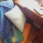 Blue quilt shown draped over a chair with a pillow in the chair pulled out from a desk