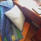 Blue quilt shown draped over a chair with a pillow in the chair pulled out from a desk