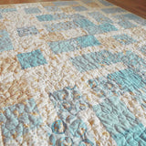 Angled view of handcrafted blue and cream baby quilt with whimsical bunny patterns