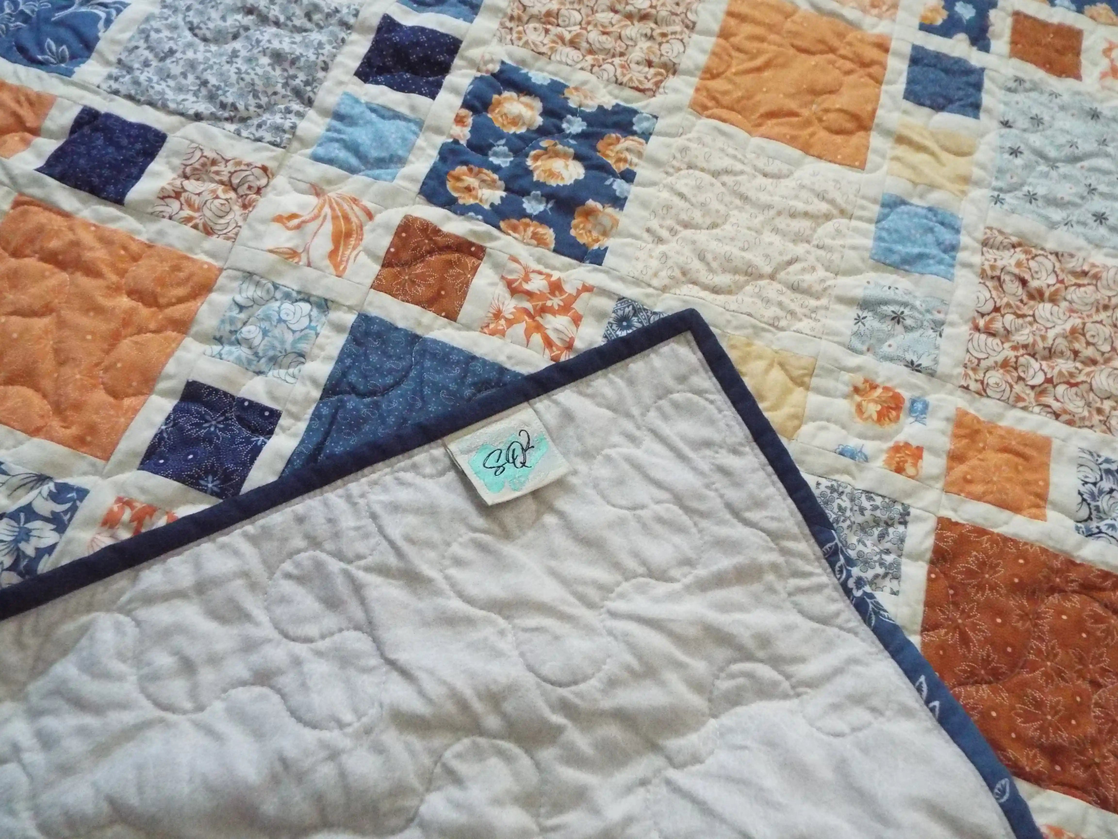 Signature SQ² Creations label and soft cotton backing showing the maker’s tag and quilt texture.