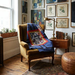 A cozy room scene with a mustard yellow armchair draped with Air Force Eagle Throw Quilt. The chair sits beside a wooden side table with a brass lamp and books, against a wall covered in framed botanical and abstract prints.