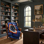 A styled home office interior with dark teal paneled walls, built-in bookshelves, a large wooden desk, a leather armchair draped with Air Force Airman Throw Quilt, and framed landscape paintings on the wall.