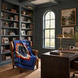 A styled home office interior with dark teal paneled walls, built-in bookshelves, a large wooden desk, a leather armchair draped with Air Force Airman Throw Quilt, and framed landscape paintings on the wall.