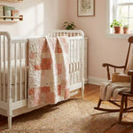 Quilt shown draped over crib in a pale pink nursery