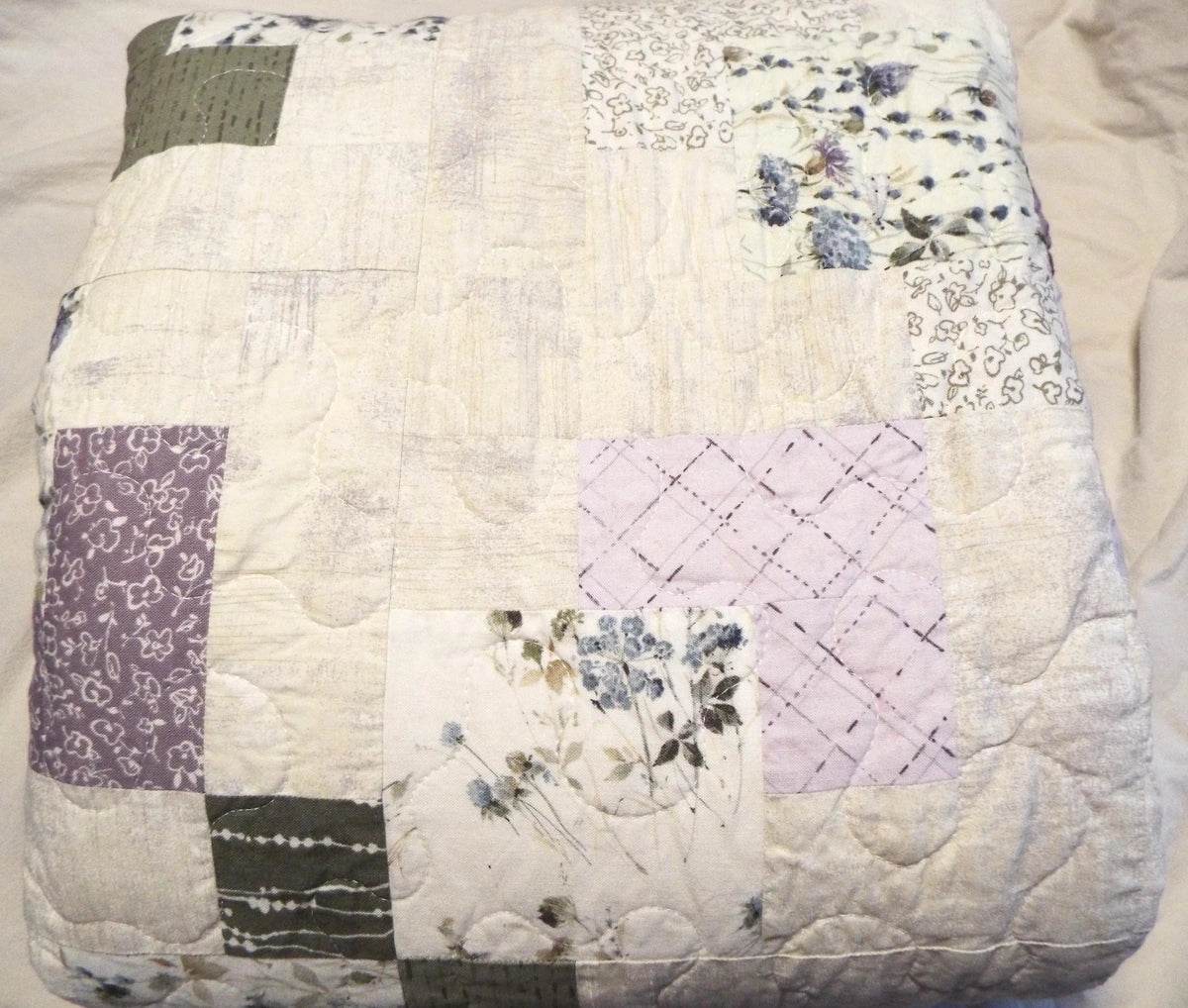 Twin sized quilt in purples and greens folded on a bed