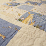 Angled close-up of a handmade quilt in blue and tan bunny fabrics, showing soft texture, neat stitching, and subtle color variations