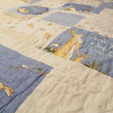 Angled close-up of a handmade quilt in blue and tan bunny fabrics, showing soft texture, neat stitching, and subtle color variations