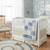 Patchwork baby quilt in soft blues, tans, and white folded over the side of a white crib in a nursery decorated with bunnies and cloud wallpaper.
