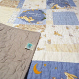 Detail view of a baby quilt with the corner gently flipped to show the gray backing and tidy binding, highlighting the handmade finish