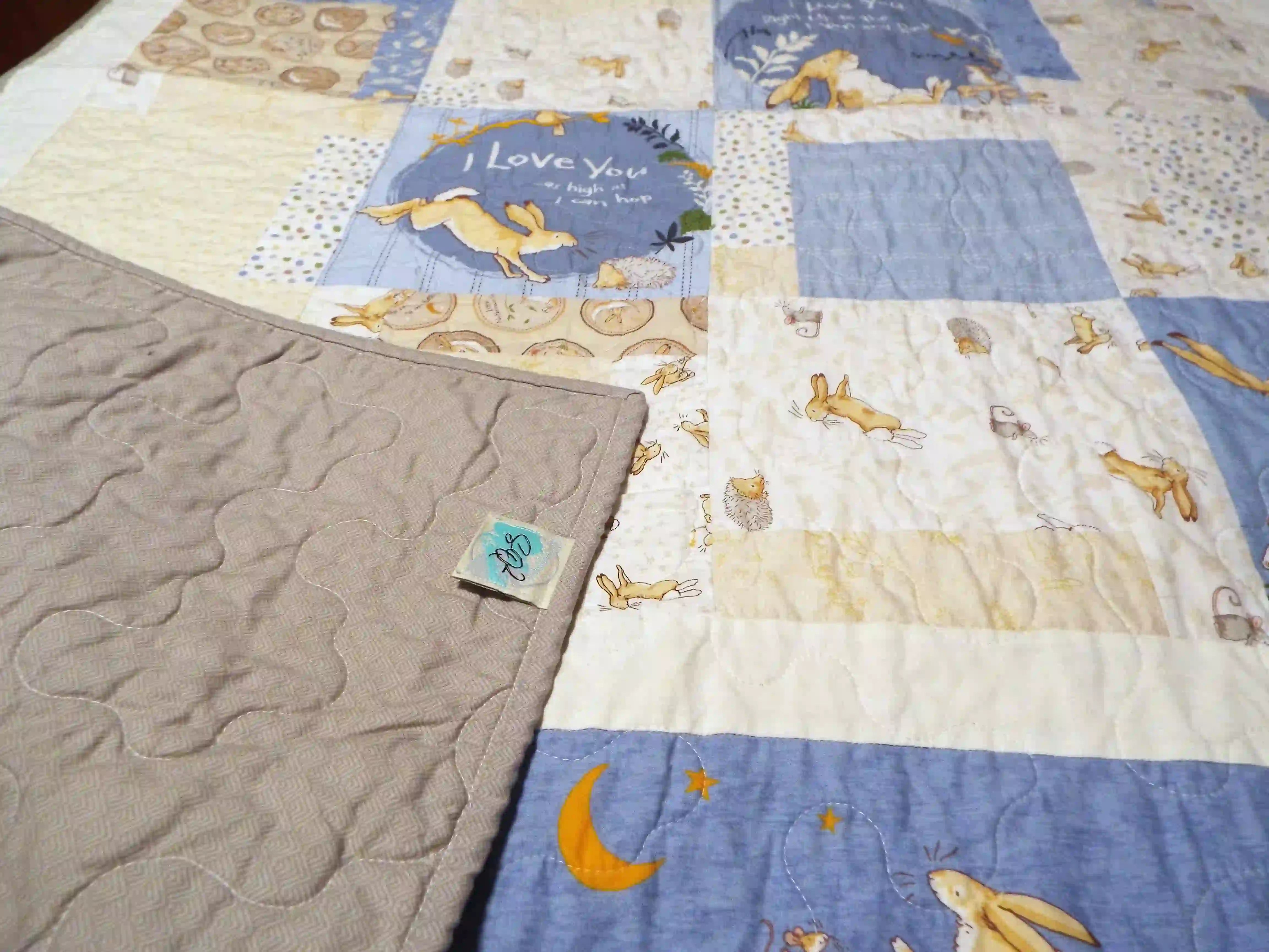 Detail view of a baby quilt with the corner gently flipped to show the gray backing and tidy binding, highlighting the handmade finish