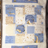 Flat lay of a handmade baby quilt with soft blue, cream, and tan bunny prints in a classic square pattern, captured in natural light on a dark gray background