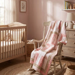 Blushing Pathways Baby Quilt shown draped over a rocking chair in a pale pink nursery.