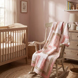 Blushing Pathways Baby Quilt shown draped over a rocking chair in a pale pink nursery.