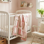 Blushing Pathways Baby Quilt shown draped over a white crib in a pale pink nursery.