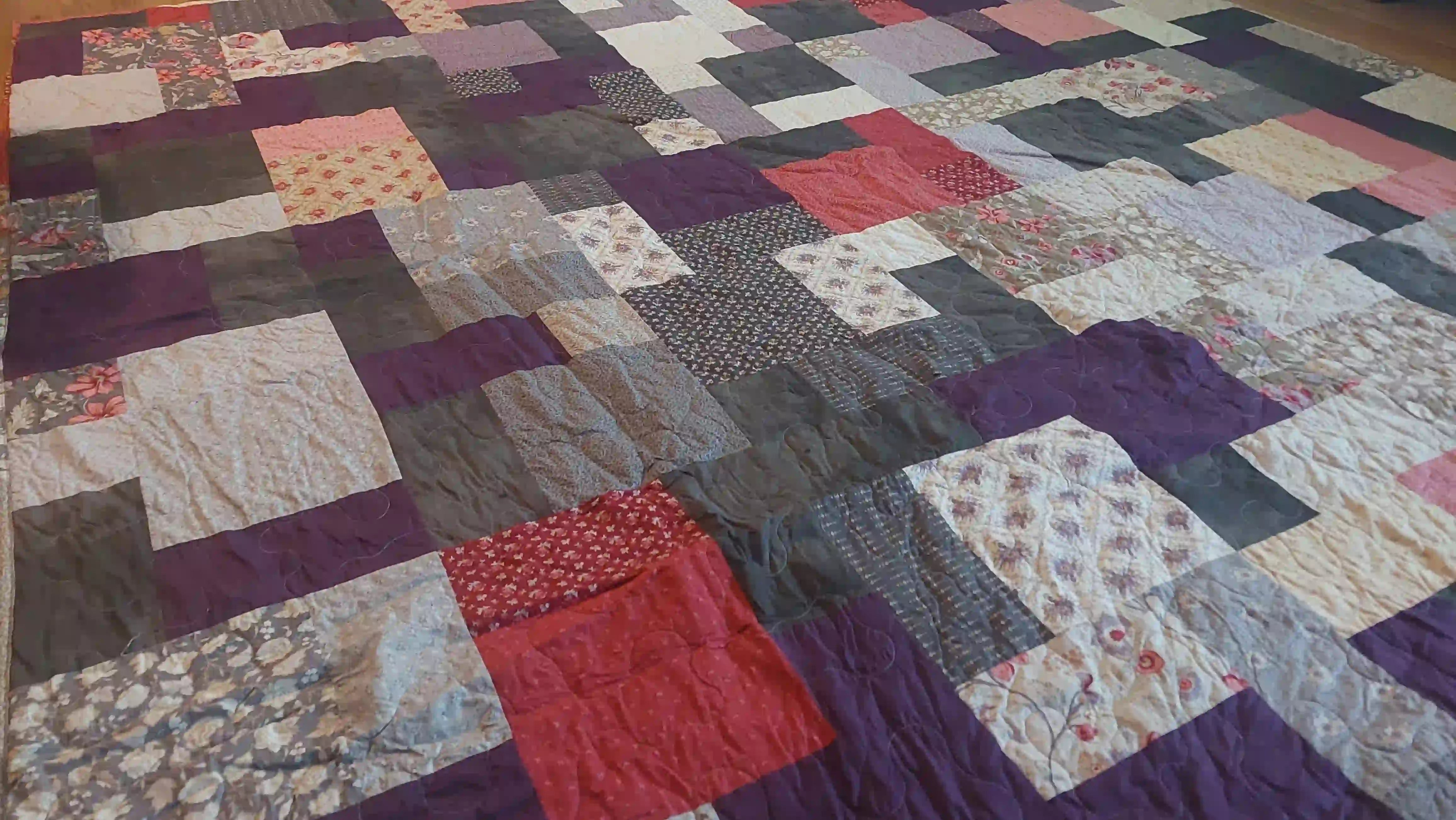 Angled lay of Bramble & Stone King quilt showing stitching and fabrics used in construction.