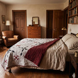 A cozy bedroom scene featuring a bed dressed with Cartographer's Notes Queen Quilt, surrounded by warm wood furniture, bookshelves, and a leather armchair.