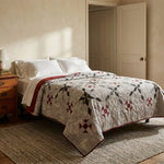 A quilted bedspread with Cartographer's Notes Queen Quilt styled on a bed in a warm, sunlit bedroom with a wooden nightstand and textured rug.