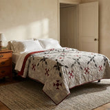A quilted bedspread with Cartographer's Notes Queen Quilt styled on a bed in a warm, sunlit bedroom with a wooden nightstand and textured rug.