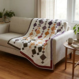 Embers at Dusk lap quilt shown draped over a neutral couch
