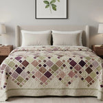 Handmade patchwork quilt in muted purples and greens styled in a modern neutral bedroom with upholstered headboard and botanical wall art.