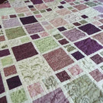 Close-up of lavender and green patchwork squares on handmade king quilt showing intricate stitching and soft cotton texture