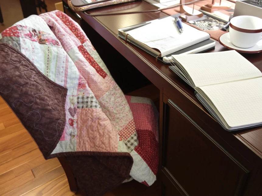 Handmade floral and hearts quilt shown draped over a chair at a desk